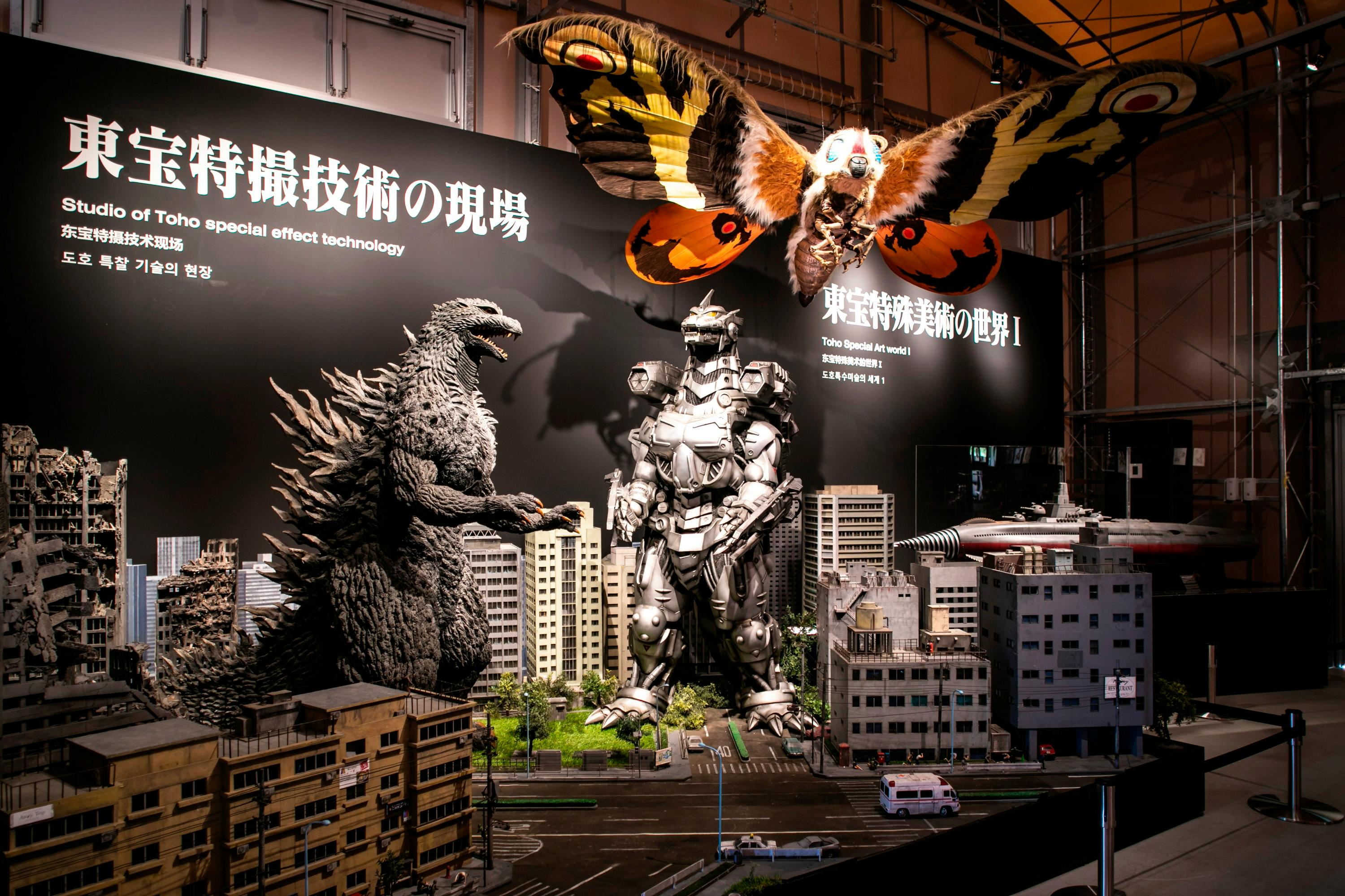 A display featuring models of Godzilla, Mechagodzilla, and Mothra over a miniature cityscape with text panels in Japanese.