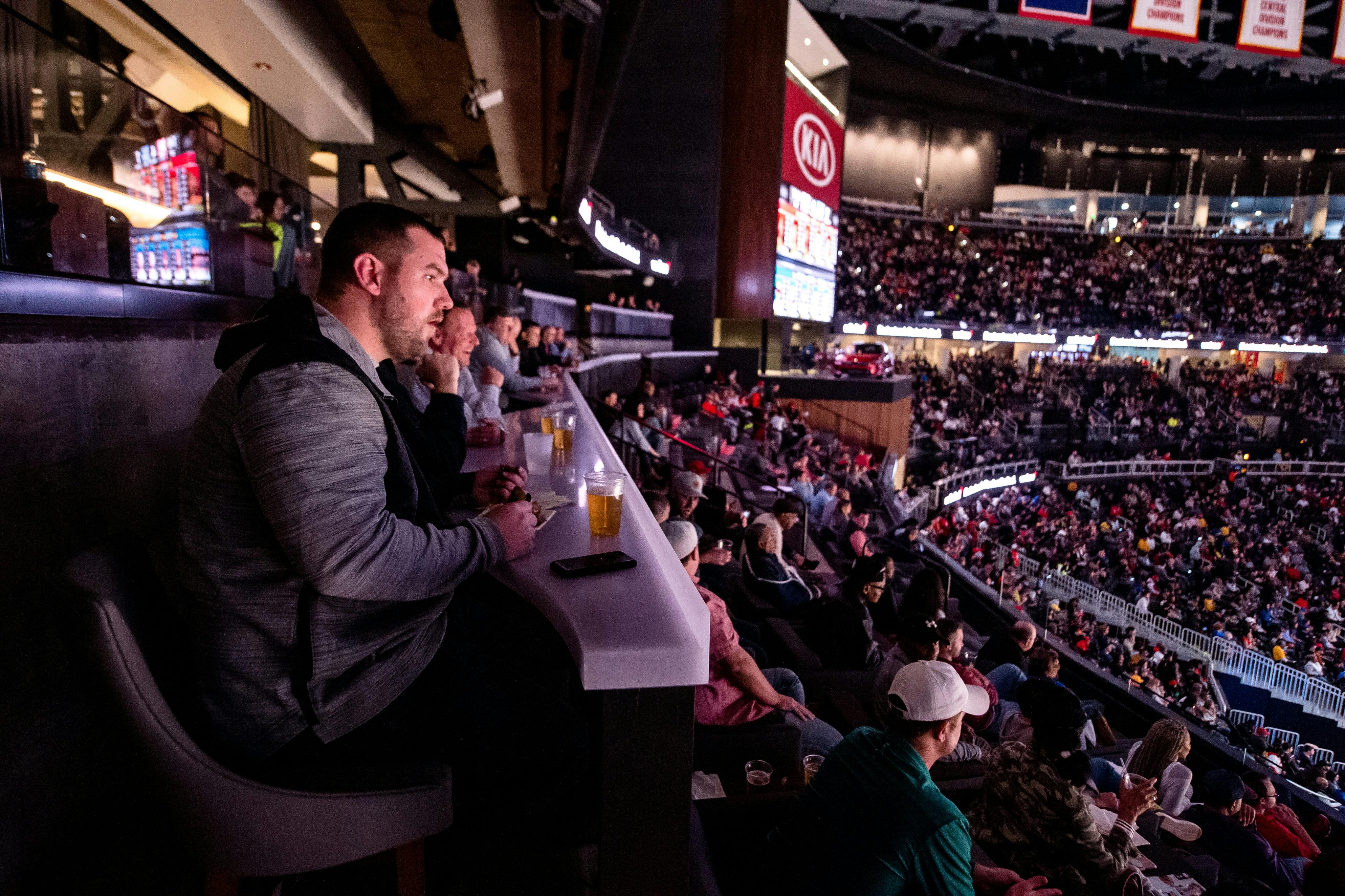 스포츠 경기장 라운지에 앉아 아래 행사를 관람하는 사람들. 음료는 앞에 있는 테이블에 있습니다.