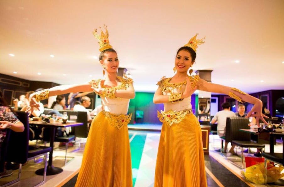 Dvě ženy v tradičních krojích tančí v restauraci s parťáky v pozadí.