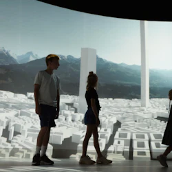 Silhuetter av tre barn som går framför en skärm som visar en futuristisk stadsbild med berg i bakgrunden.