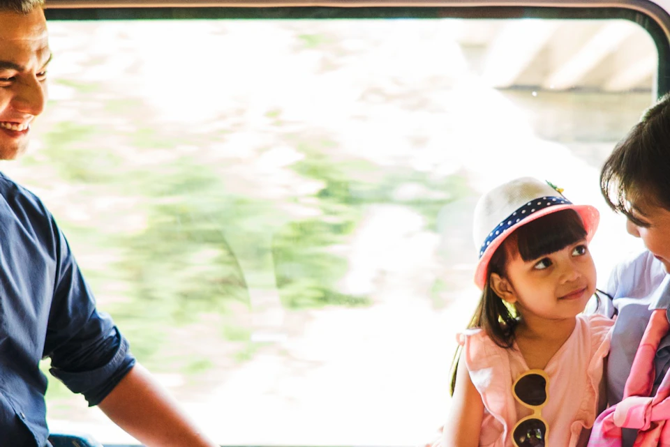 A family sits together on a train, smiling and interacting, with sunlight streaming through the window.