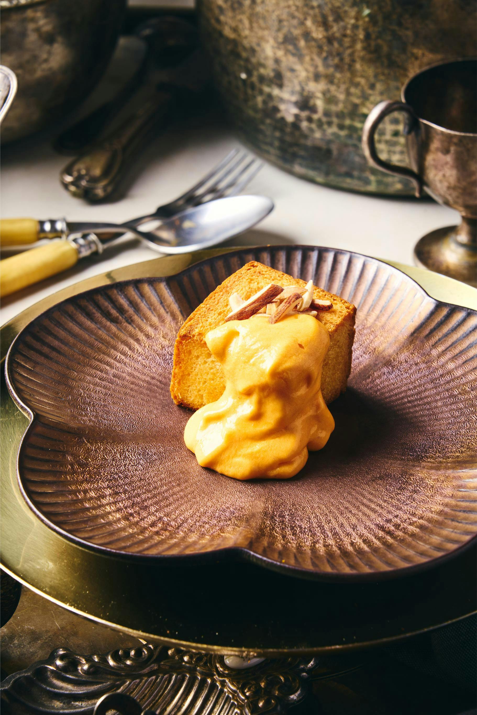 A dessert of cake topped with orange-hued cream and garnished with almond slivers, served on a decorative plate.