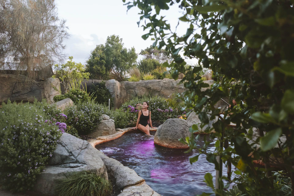 Woman sitting on edge of geothermal rockpool with legs submerged in thermal waters