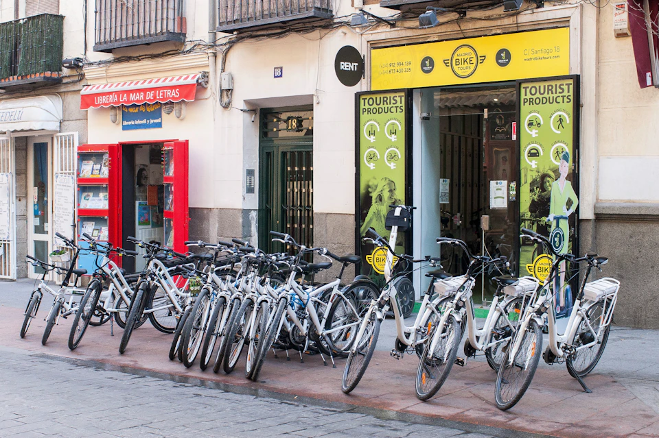 A row of bicycles for rent outside a shop labeled "Tourist Products" with a red storefront next door.