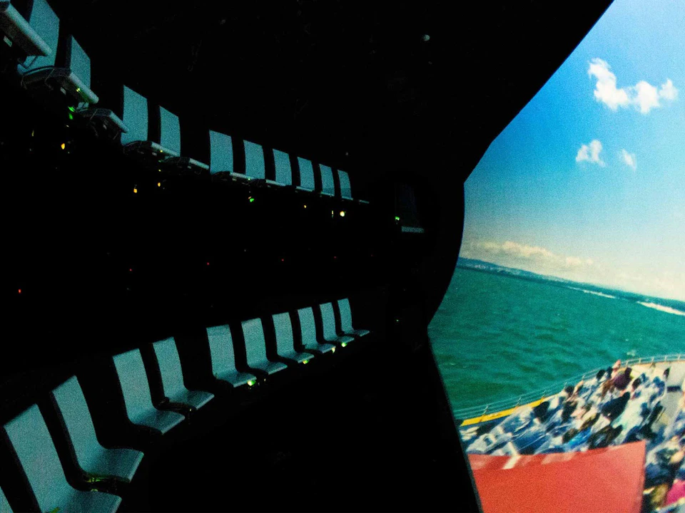 Rows of empty seats facing a large, curved screen displaying a scene of the ocean under a blue sky.