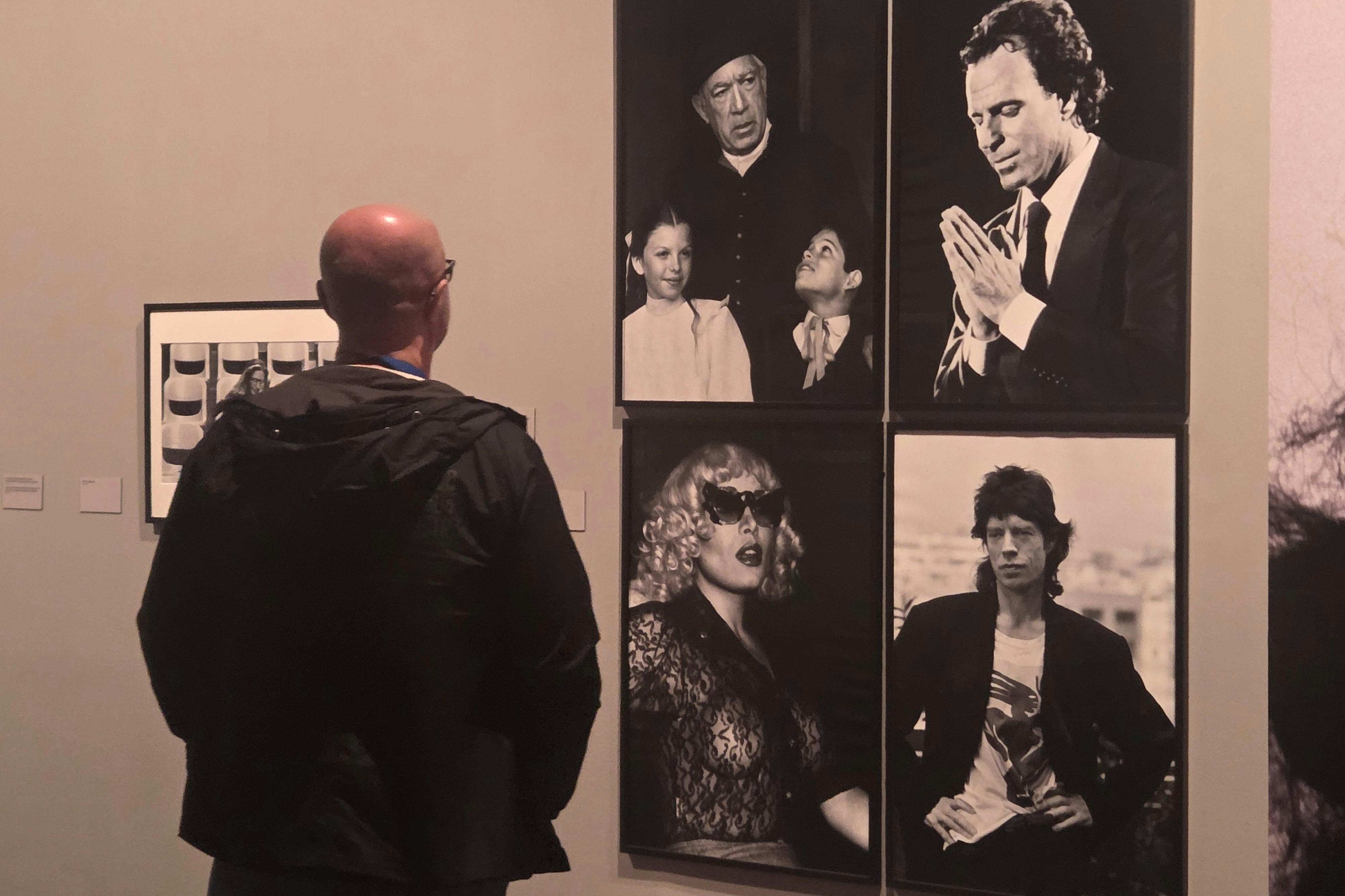 Uma pessoa vê quatro retratos a preto e branco expostos numa parede, cada um com um indivíduo ou grupo em poses diferentes.