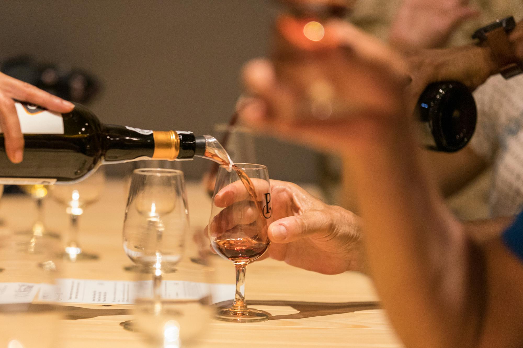 テイスティングイベントでは、手でロゼワインのグラスを注ぎ、軽い木製のテーブルの上に空のグラスと半分満たされたグラスを置きます。