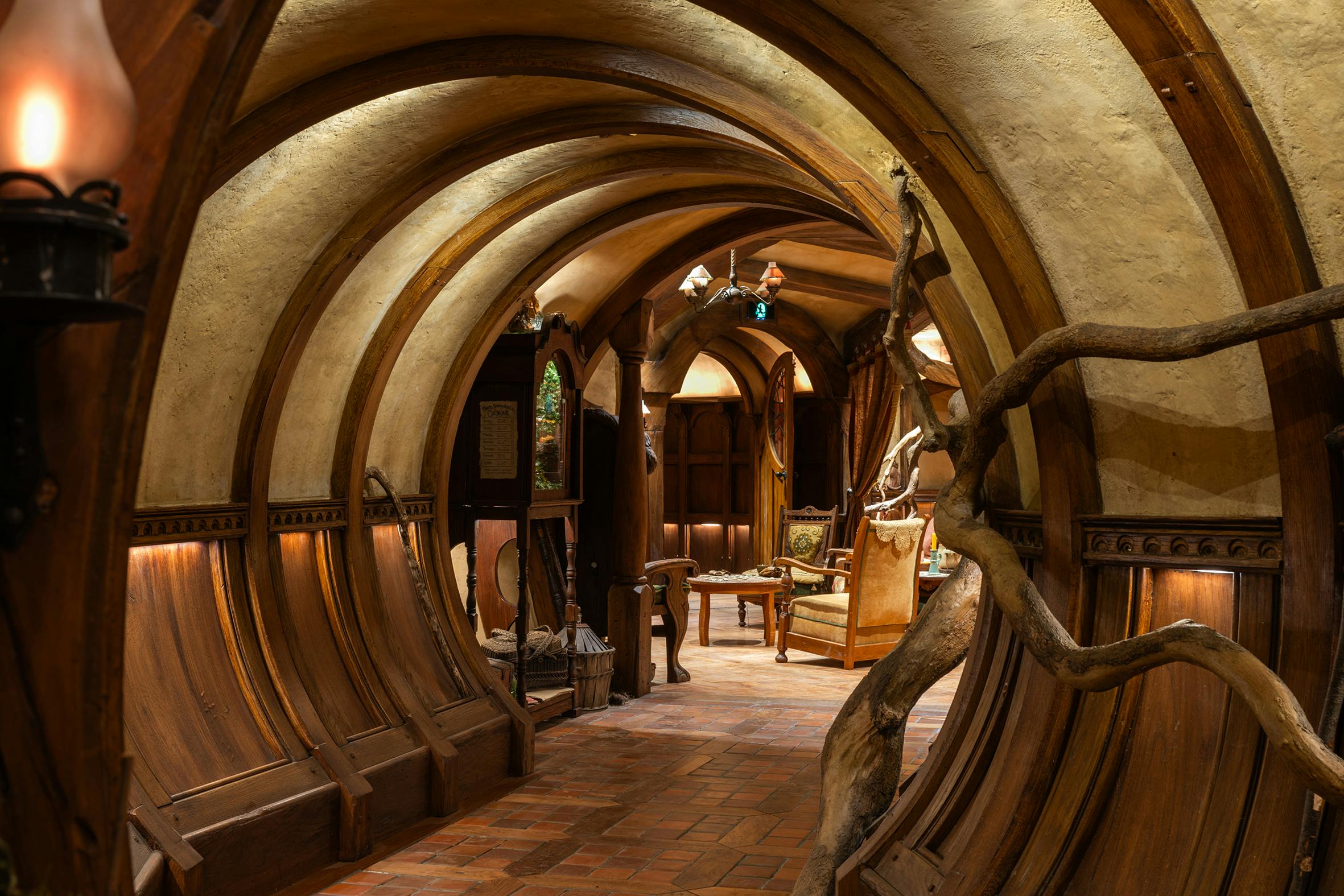 A cozy interior with arched wooden beams, tiled floor, tree-like decor, and a sitting area with chairs and warm lighting.