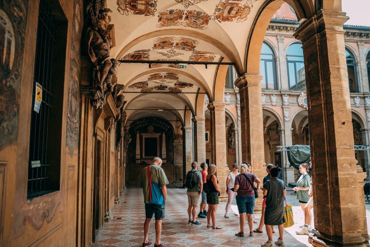 Tourists standing and walking in an ornately decorated historical hallway with arched ceilings and detailed paintings.