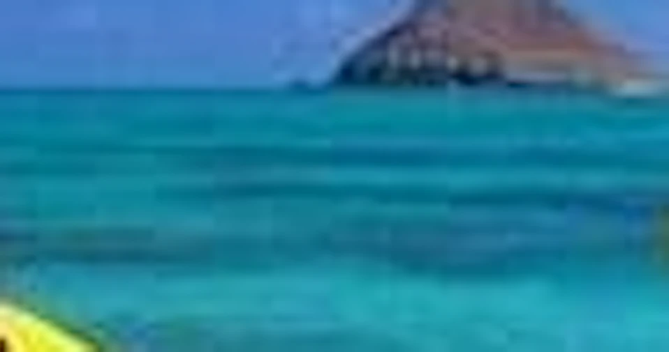Two people kayaking on a yellow kayak in clear turquoise water with small islands visible in the background under a blue sky.