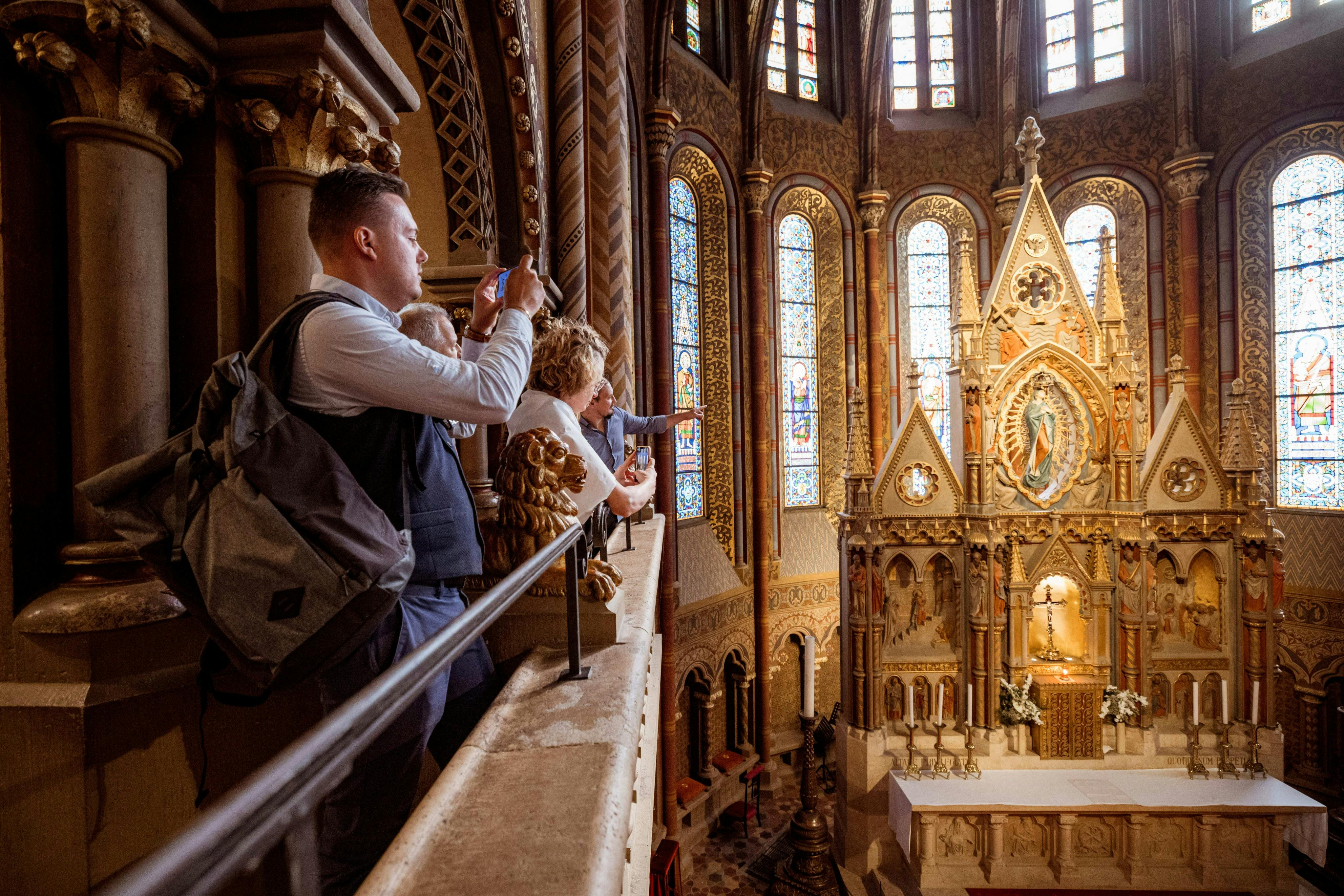 People standing on an indoor balcony of a cathedral, observing the ornate interior and stained-glass windows.