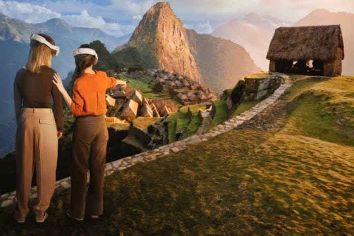 Dos personas con cascos de RV exploran una recreación digital de Machu Picchu, con una cabaña de paja y montañas al fondo.
