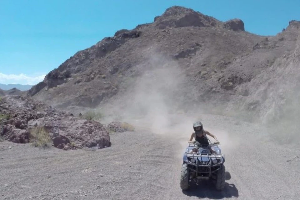 A person riding an ATV on a dirt trail in a rocky desert landscape under a clear blue sky.
