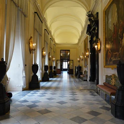 Elegant hall med välvt tak, stora målningar, guldlampor, höga urnor, rutigt golv och ljus som strömmar genom höga fönster.