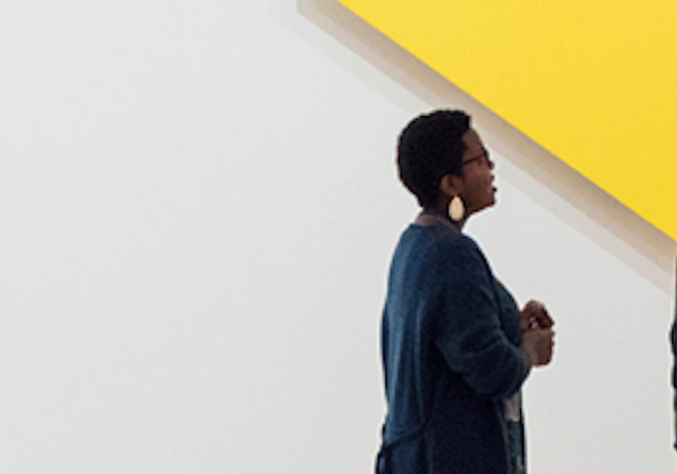 People observing abstract geometric paintings in a modern, well-lit art gallery.