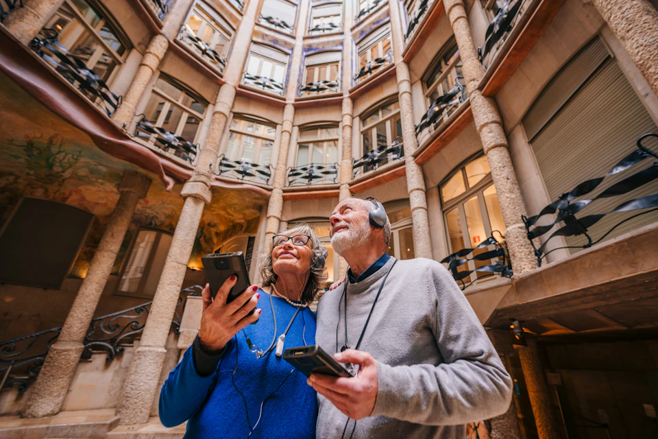 A man and woman with audio guides admire the architecture of a circular courtyard with ornate columns and balconies.