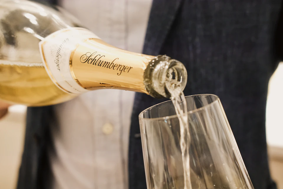A bottle of Schlumberger champagne being poured into a glass, with a person in a suit jacket visible in the background.