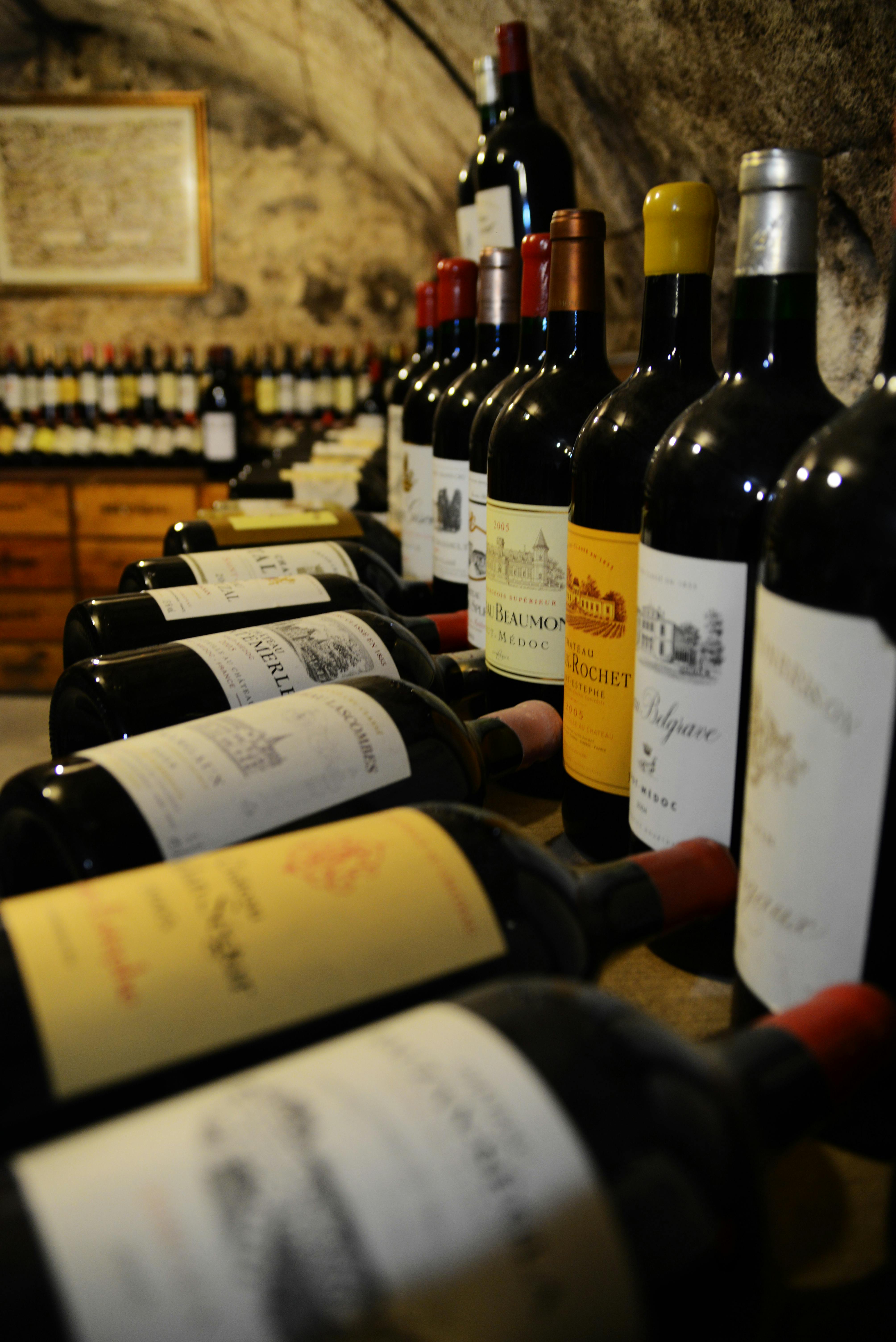 Řada lahví vína vystavená na dřevěných regálech v obchodě s dalšími lahvemi na policích v pozadí.