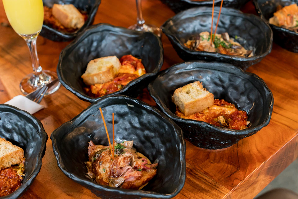 Black bowls containing food garnished with bread slices and skewers are arranged on a wooden table.