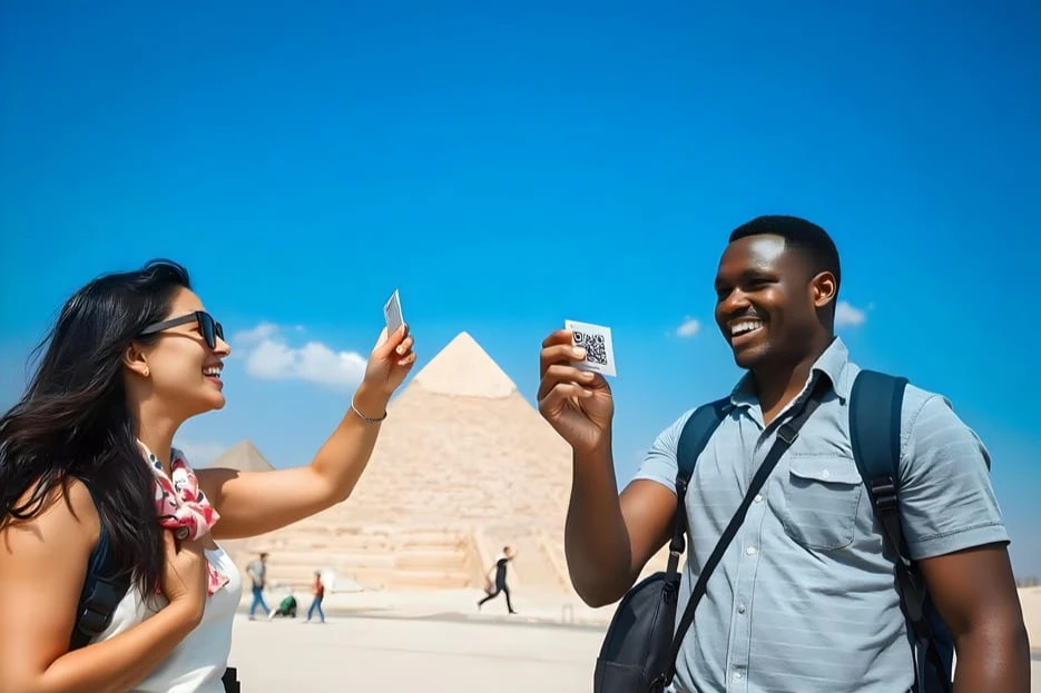 A man stands smiling near pyramids, holding up a card with a QR code. Another person’s hand holding a card is also visible.