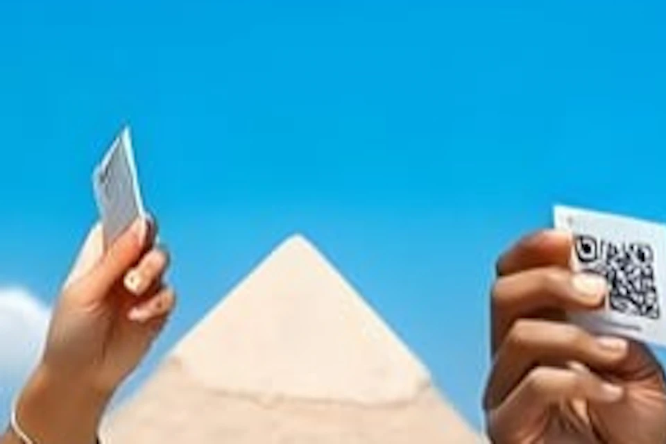 A man stands smiling near pyramids, holding up a card with a QR code. Another person’s hand holding a card is also visible.