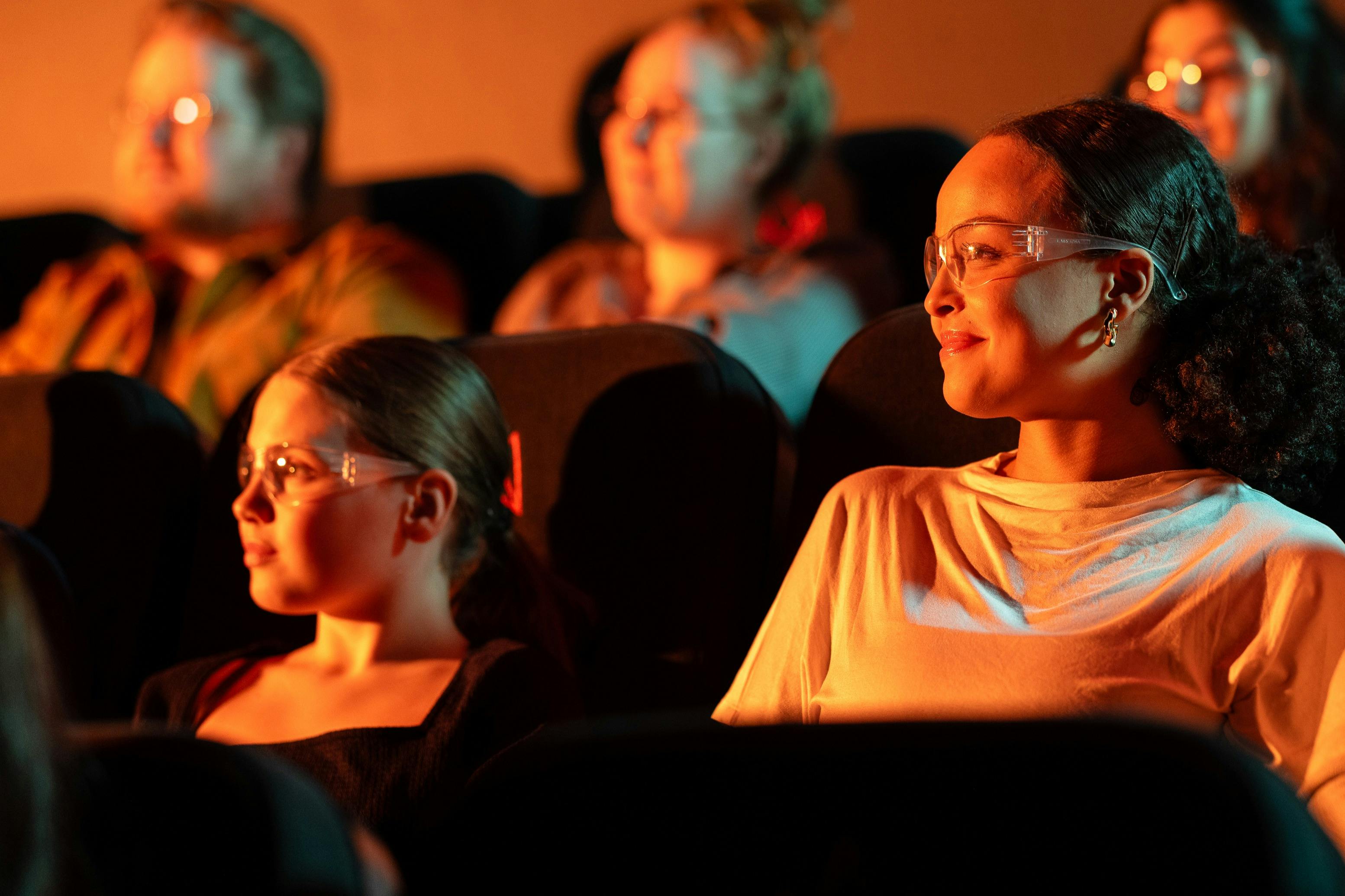 Ένα κορίτσι και η μητέρα της παρακολουθούν το Lava Show. Φορούν προστατευτικά γυαλιά. Το κοινό στο παρασκήνιο.