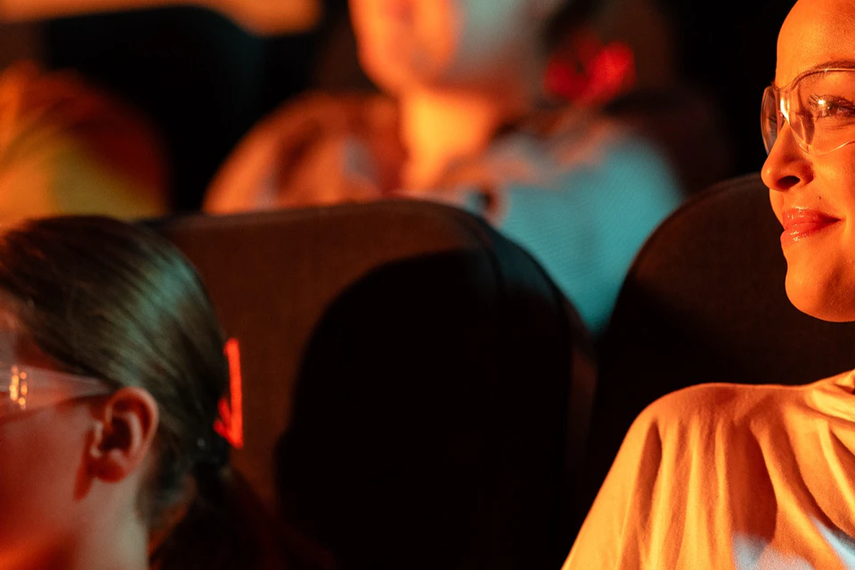 A girl and her mother watch the Lava Show. They are wearing safety goggles. Audience in the background.