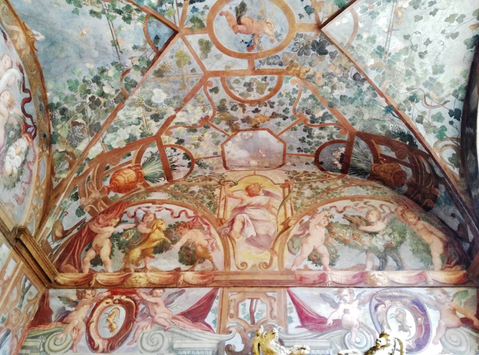 Intricately painted ceiling with cherubs, foliage, and mythical figures in vibrant colors, depicting an elaborate classical scene.