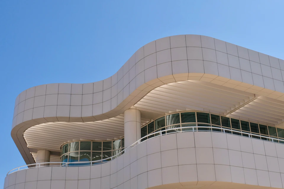 A modern building with curved, white-tiled architecture against a clear blue sky. Rounded windows and columns are also visible.