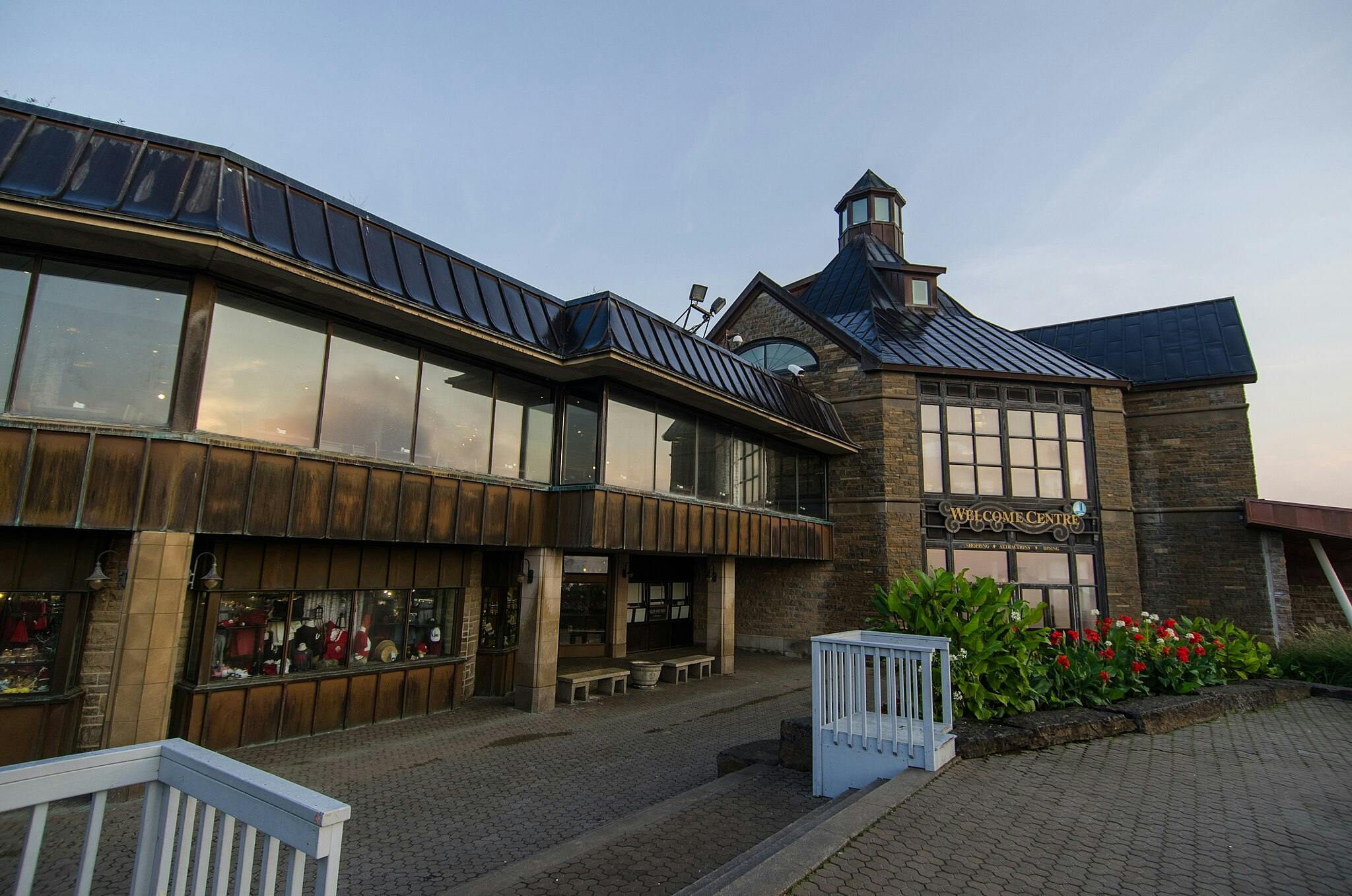 A welcome center with large windows, stone structure, and flower bed in front under a twilight sky.