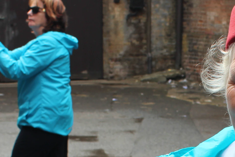 An older woman in a red cap and blue coat holds a photo while talking. Two women in the background take photos.