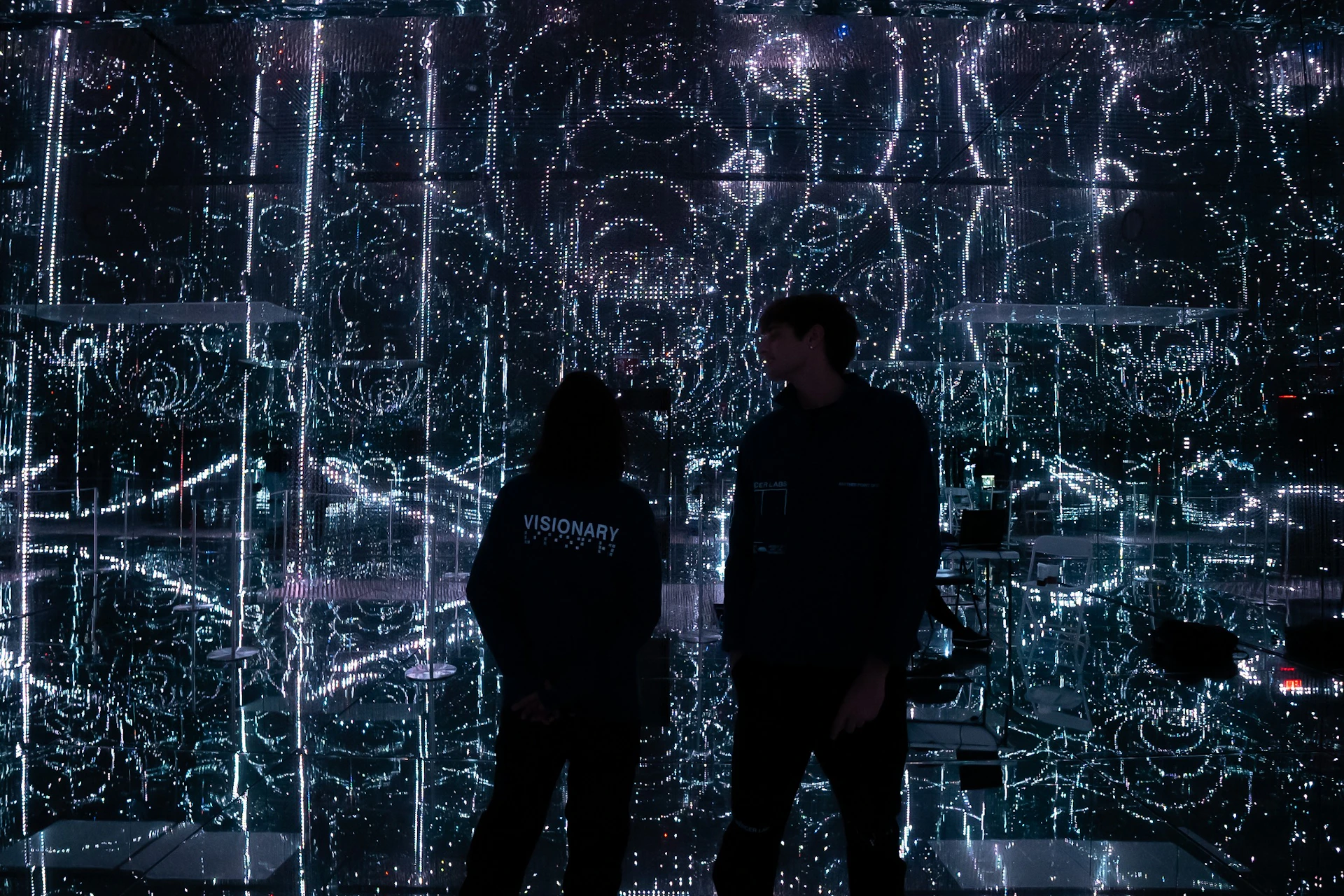 Two people stand in a room with walls covered in intricate, glowing patterns of light.