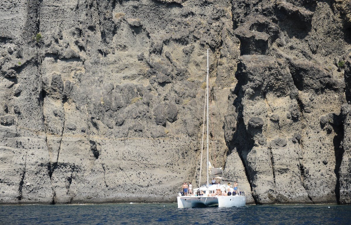 一艘双体船，船上的人漂浮在一个巨大的岩石悬崖边。