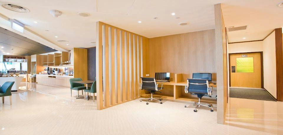 A modern office space with wooden partitions, two desks with computers and chairs, and a seating area in the background.