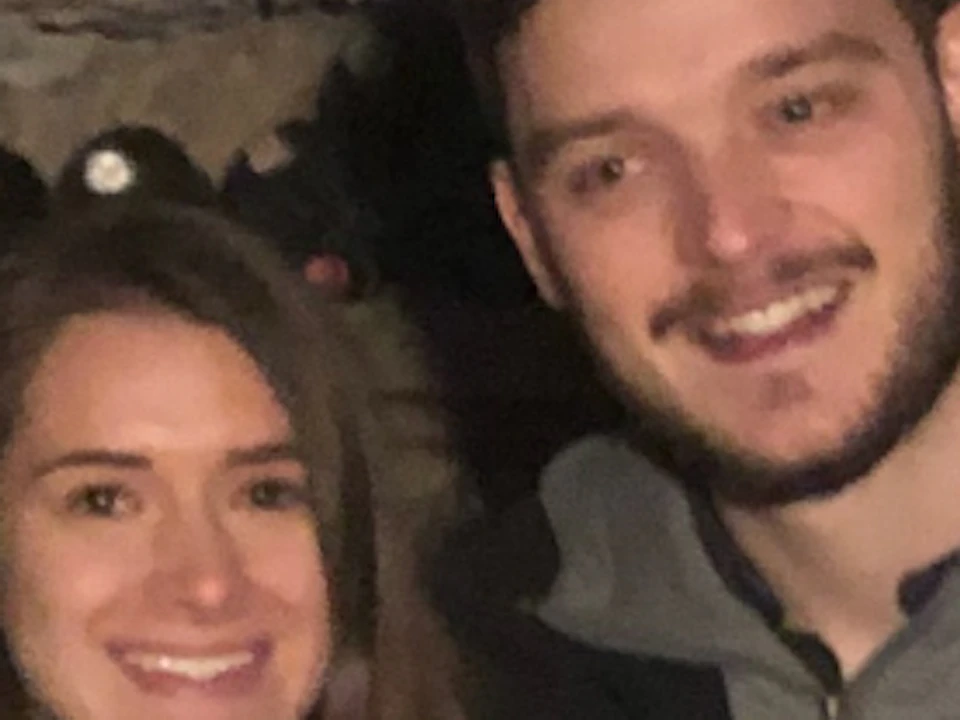 Two people standing in a wine cellar, surrounded by shelves filled with bottles of wine.