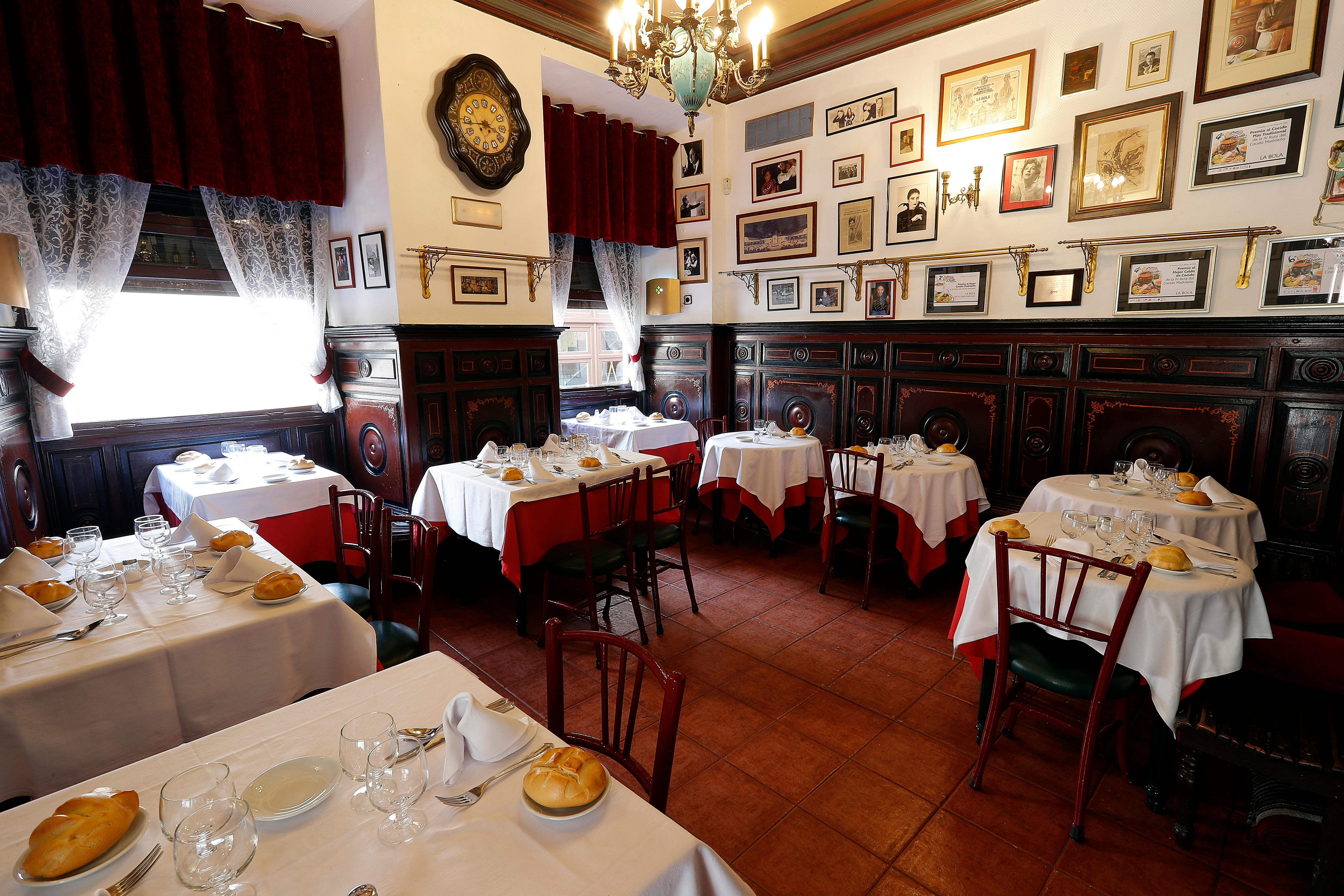 Ein gemütliches Restaurant mit gerahmten Bildern an den Wänden, weißen Tischtüchern mit roten Akzenten, gedeckten Tischen und Holzstühlen.