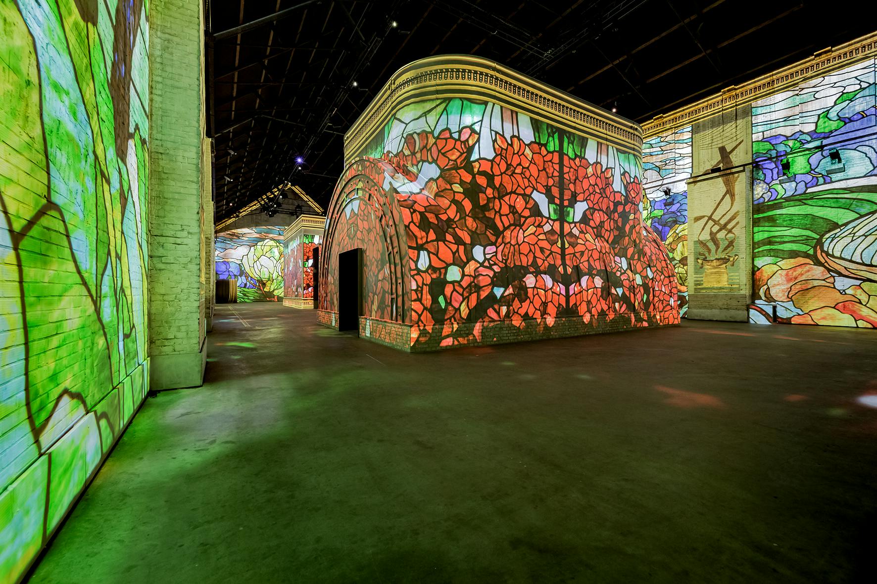 Deux personnes marchant à l'intérieur d'une exposition d'art immersif présentant des projections vibrantes à grande échelle d'une scène de jardin.