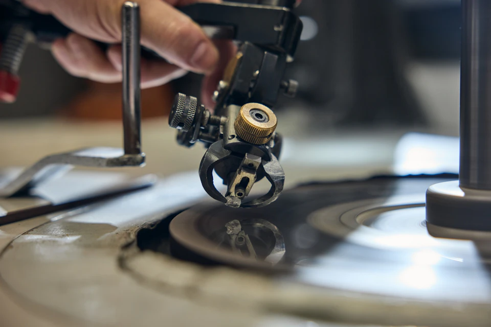 Close-up of a hand operating a vinyl record cutting lathe, with the cutting head working on a blank disc.