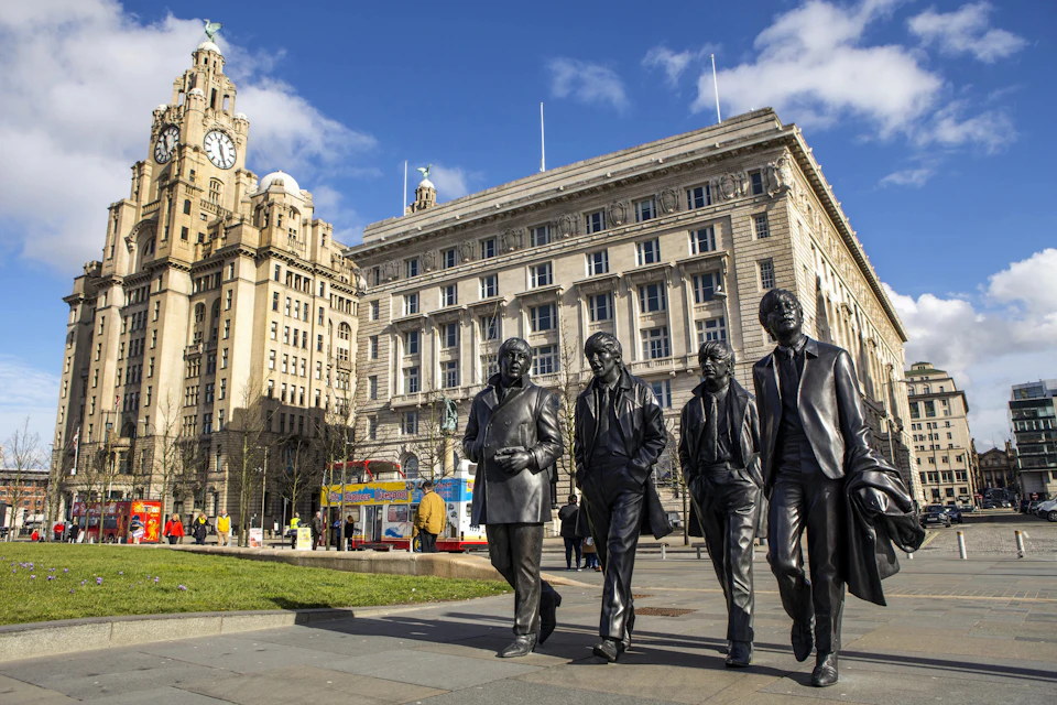 Four bronze statues of men walking, set in a plaza with large historical buildings and a few people in the background.