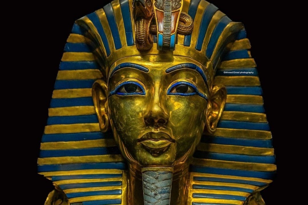 图坦卡蒙金色面具，黑色背景上饰有蓝色和金色条纹头饰和复杂的面部细节。