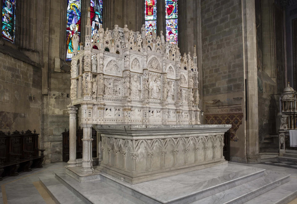 Intricately carved stone altar with religious figures and scenes, set against stained glass windows inside a church.