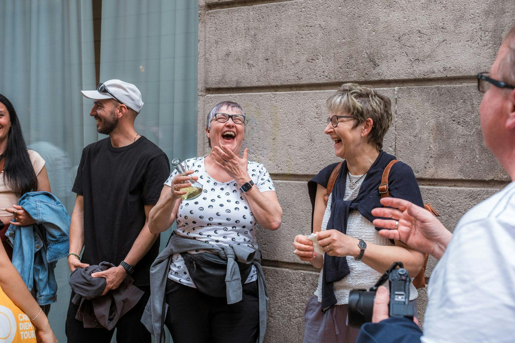 Um grupo de adultos ao ar livre, a rir e a divertir-se, com um muro de pedra e uma janela de vidro ao fundo.