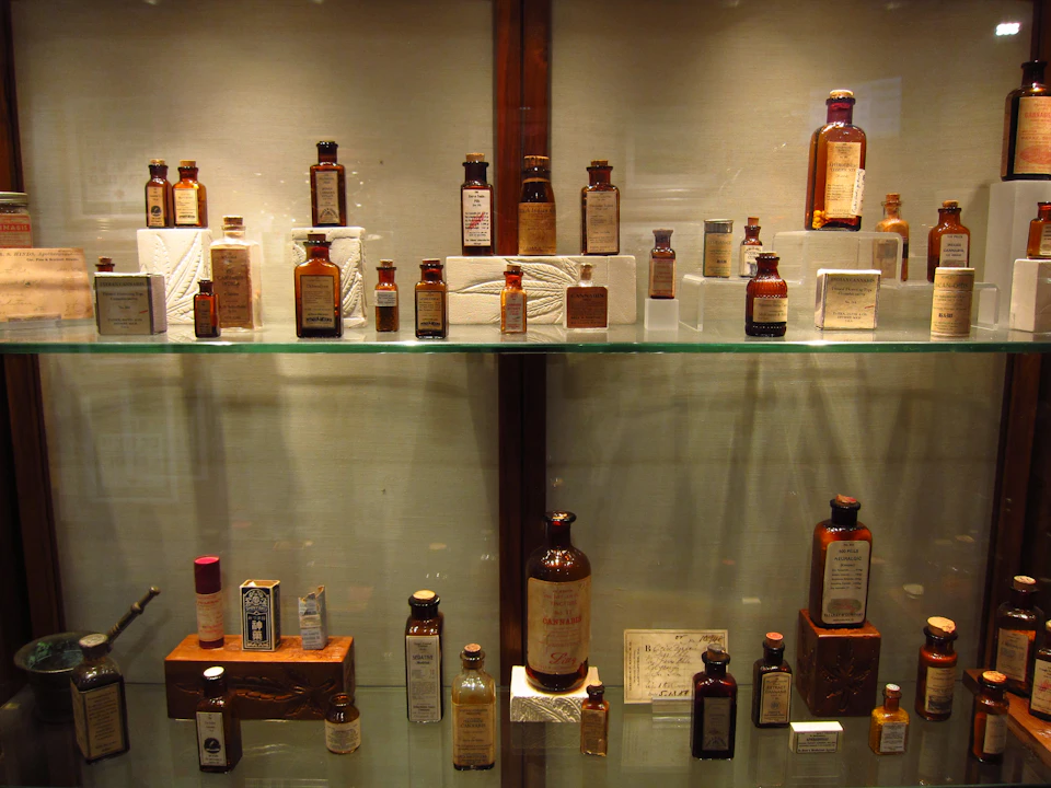 Various vintage medicine bottles and packages arranged on glass shelves in a display case.