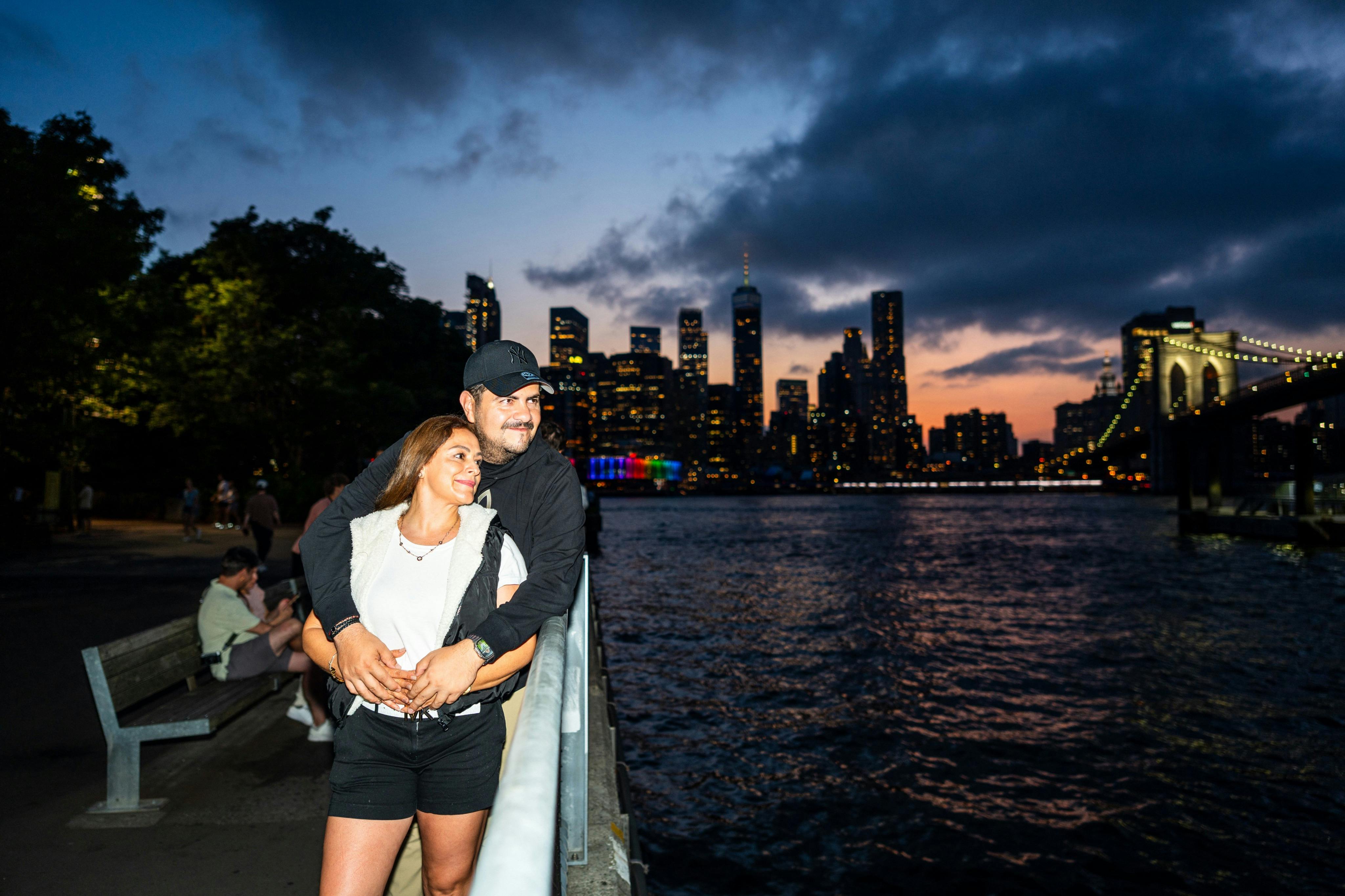 워터프론트 레일 근처에서 사람들이 벤치에 앉아 도시의 스카이라인을 바라보며 황혼을 맞이하고 있습니다.