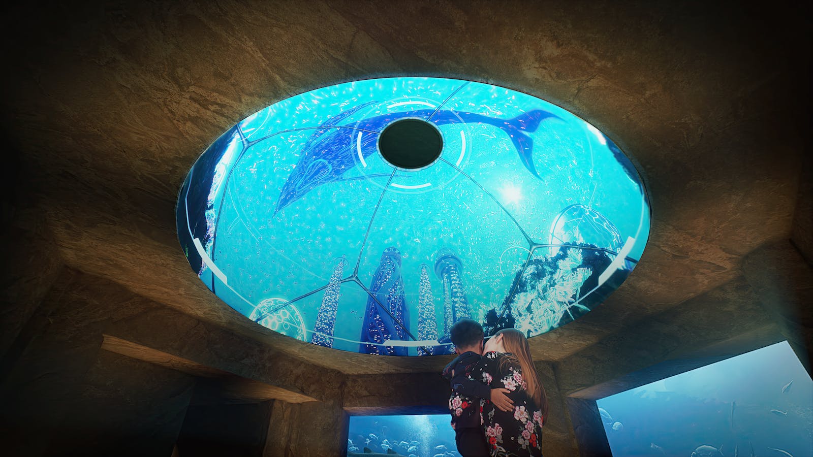 一对夫妇在一个大玻璃穹顶下拥抱，露出水下场景，上面有鲸鱼、珊瑚和海洋生物。