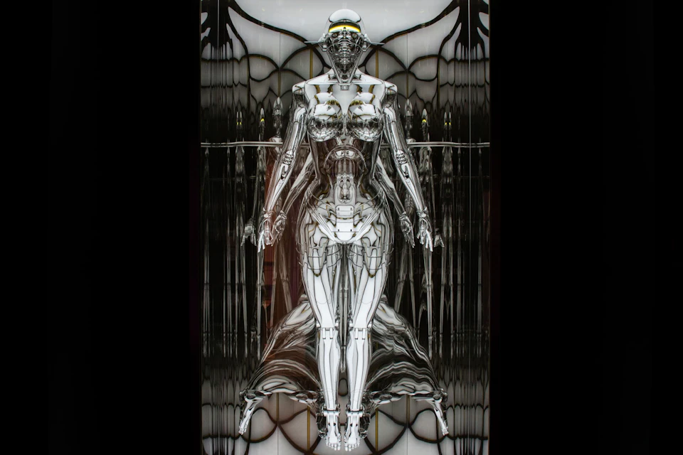 A futuristic humanoid robot with a metallic, reflective surface stands against a symmetrical, abstract background.