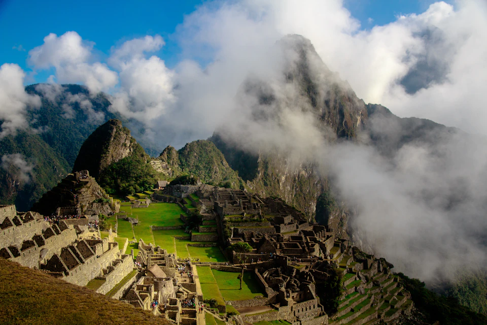 Ancient stone ruins of Machu Picchu amidst green terraces and steep mountains, partially shrouded in clouds.