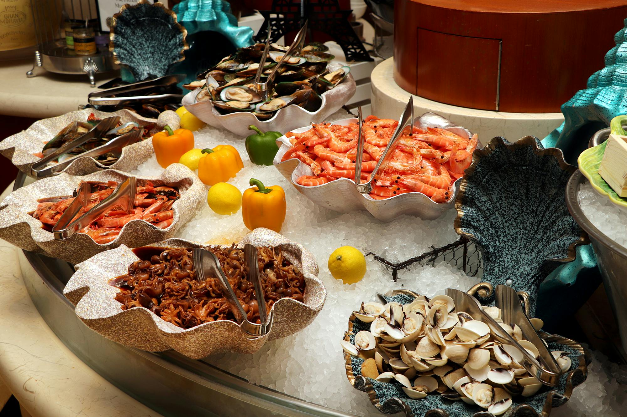 Seafood buffet display with clams, shrimp, octopus, and mussels arranged on ice with decorative shells and garnishes.
