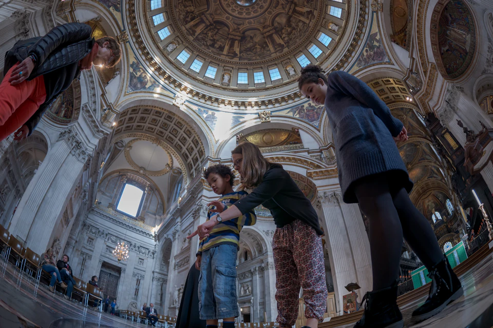 A group of people standing inside a large ornate building with a decorated dome ceiling and intricate architectural details.