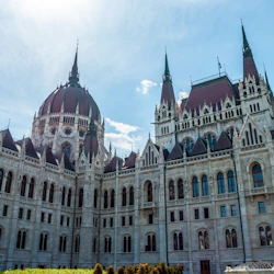 Utsmyckad byggnad med spetsiga torn och en central kupol under en molnig himmel, med välvda fönster och detaljerade arkitektoniska element.